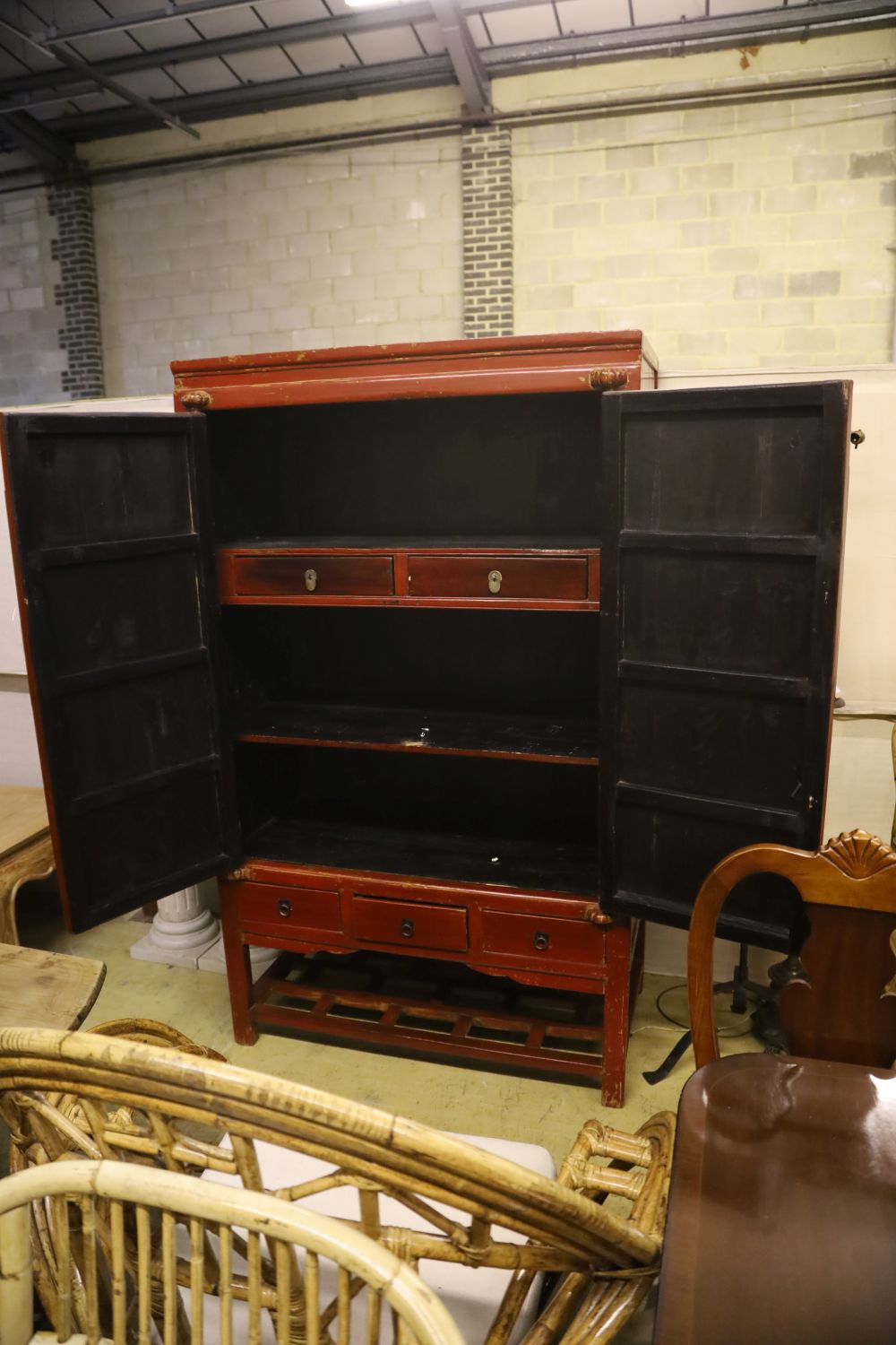 A Chinese two-door brass-mounted red-lacquered cupboard fitted three short drawers over an open shelf, width 110cm, depth 60cm, height